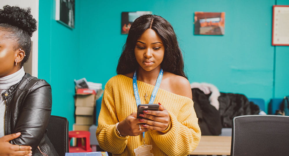 Lady wearing a yellow jumper, looking very serious,  using her phone.