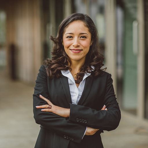 A female MBA student stands with her arms folded and looking confidently at the camera in front of the Essex Business School Building.