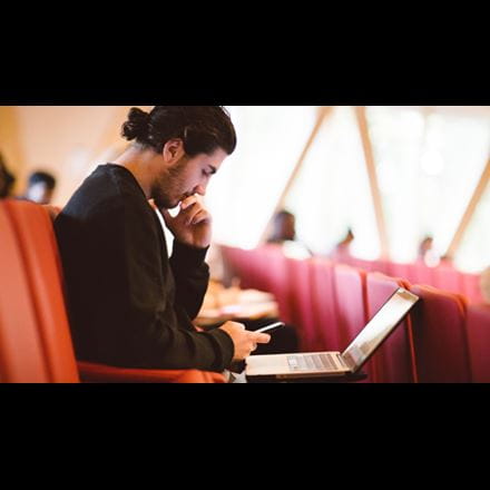 Image of a male student using both his laptop and phone simultaneously 
