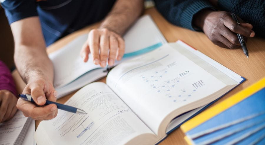 Image of people working together over a collection of textbooks on a desk