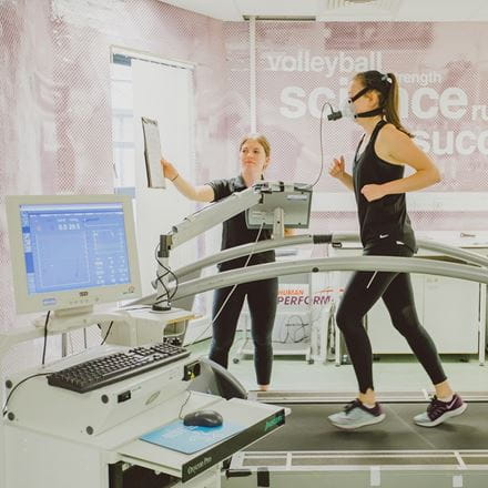 A runner on a treadmill wearing an oxygen mask, while someone holds up a clipboard in front of them.