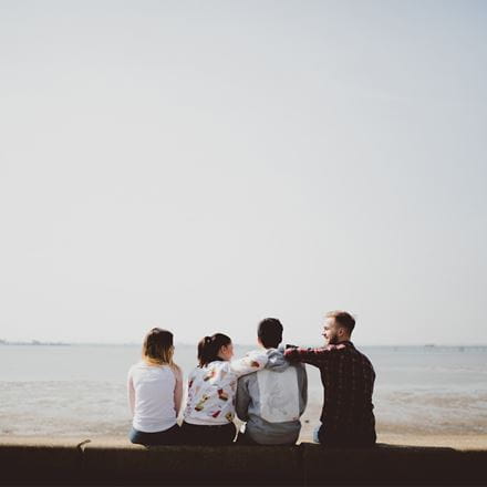 Four students sitting beside the beach in Southend facing away from the camera out towards the sea