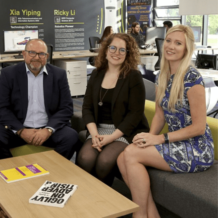 One male and two females of the Essex Startups team sitting on a sofa and smiling at the camera