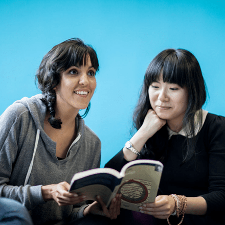 Two girls looking at a book the background is blue